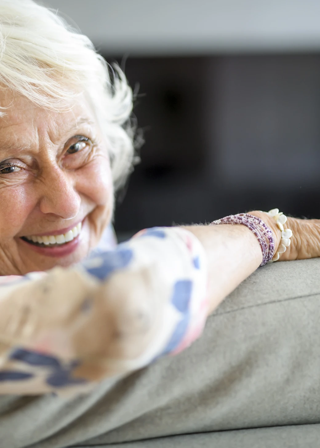 An beautiful senior woman sitting on her sofa looking over her shoulder and smiling at the camera