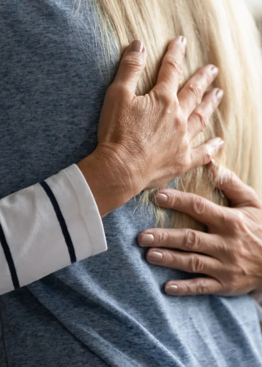 Close up shot of two people hugging, showing hands on a person's back