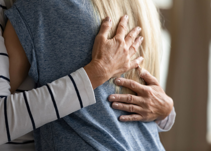 Close up shot of two people hugging, showing hands on a person's back