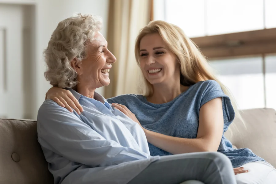 Happy young woman embracing her middle aged mother, sitting and smiling together on a comfortable sofa