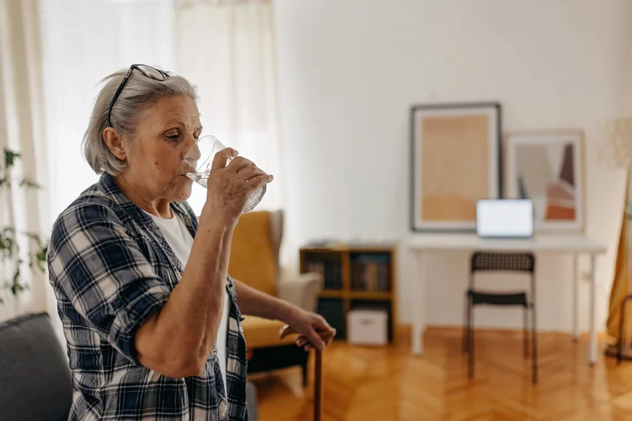 Older woman drinking a glass of water at home to keep her hydration levels up