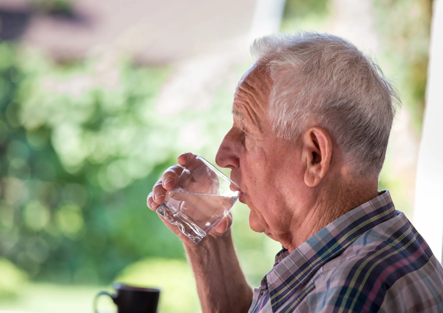 Older man drinking a glass of water at home to keep his hydration levels up