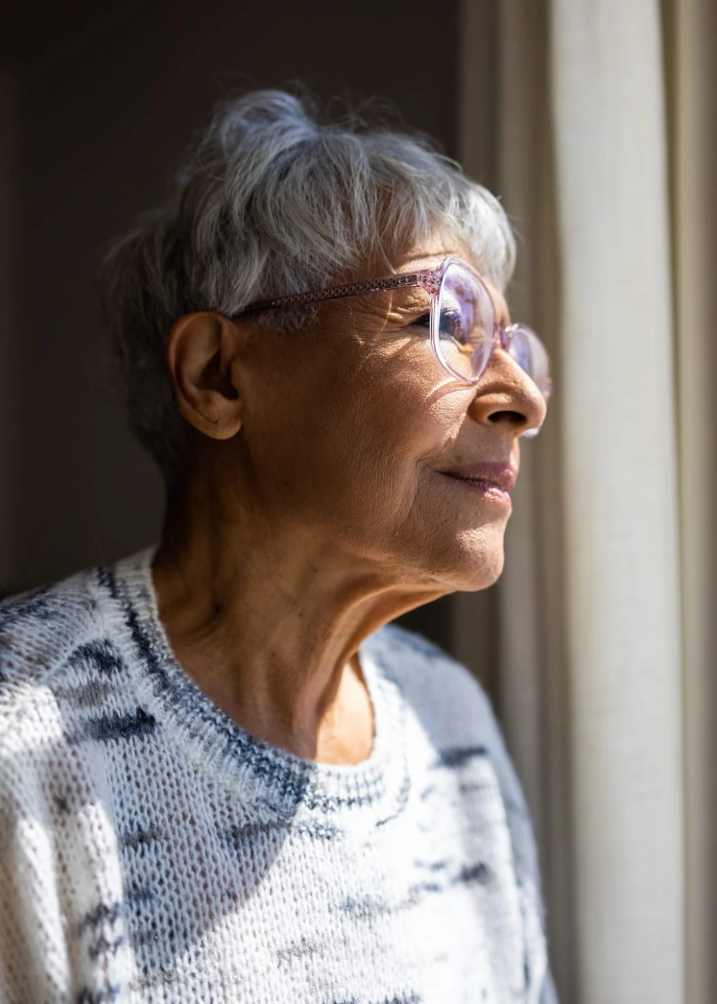 Senior woman with glasses looking out the windows of her home