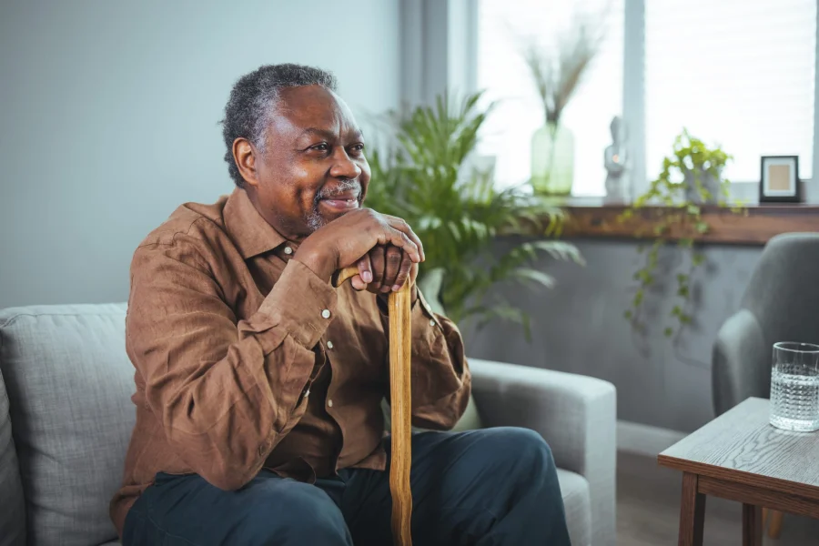 Thoughtful elderly man sitting alone at home with his walking cane.