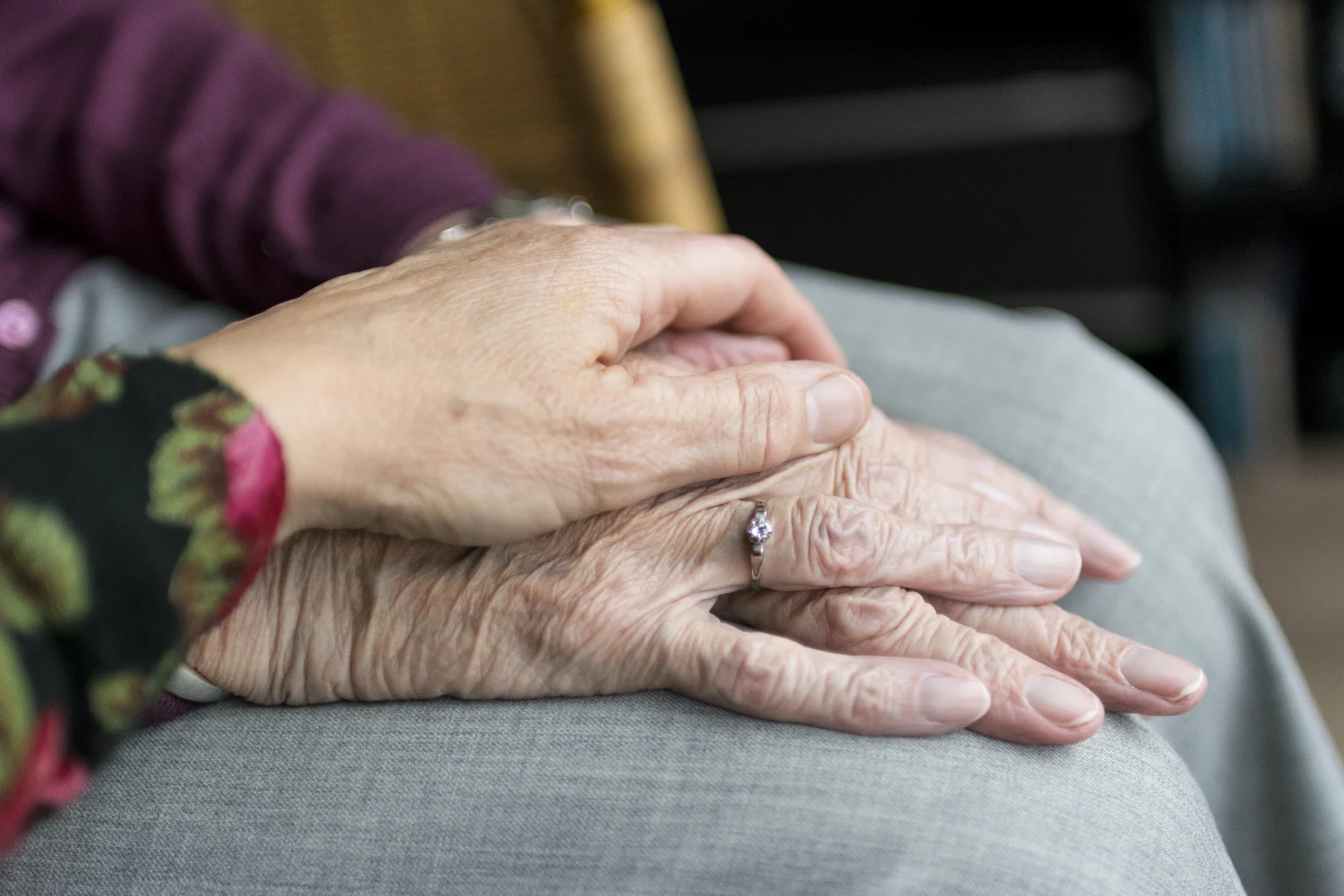 Close up of elderly hands being comforted by a carer at home