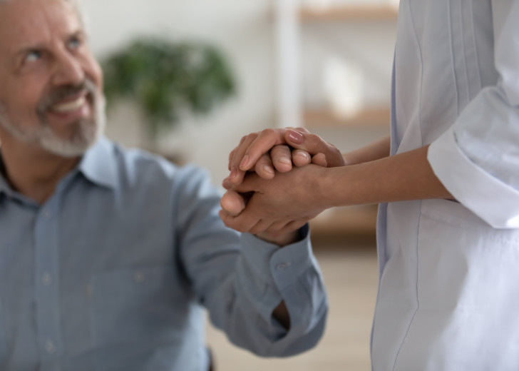 At home visiting care - a close up of a nurse holding hands with a patient at home