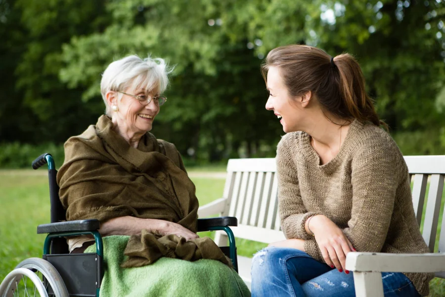 Young woman and senior woman in a wheelchair sit together in a park and share a joke